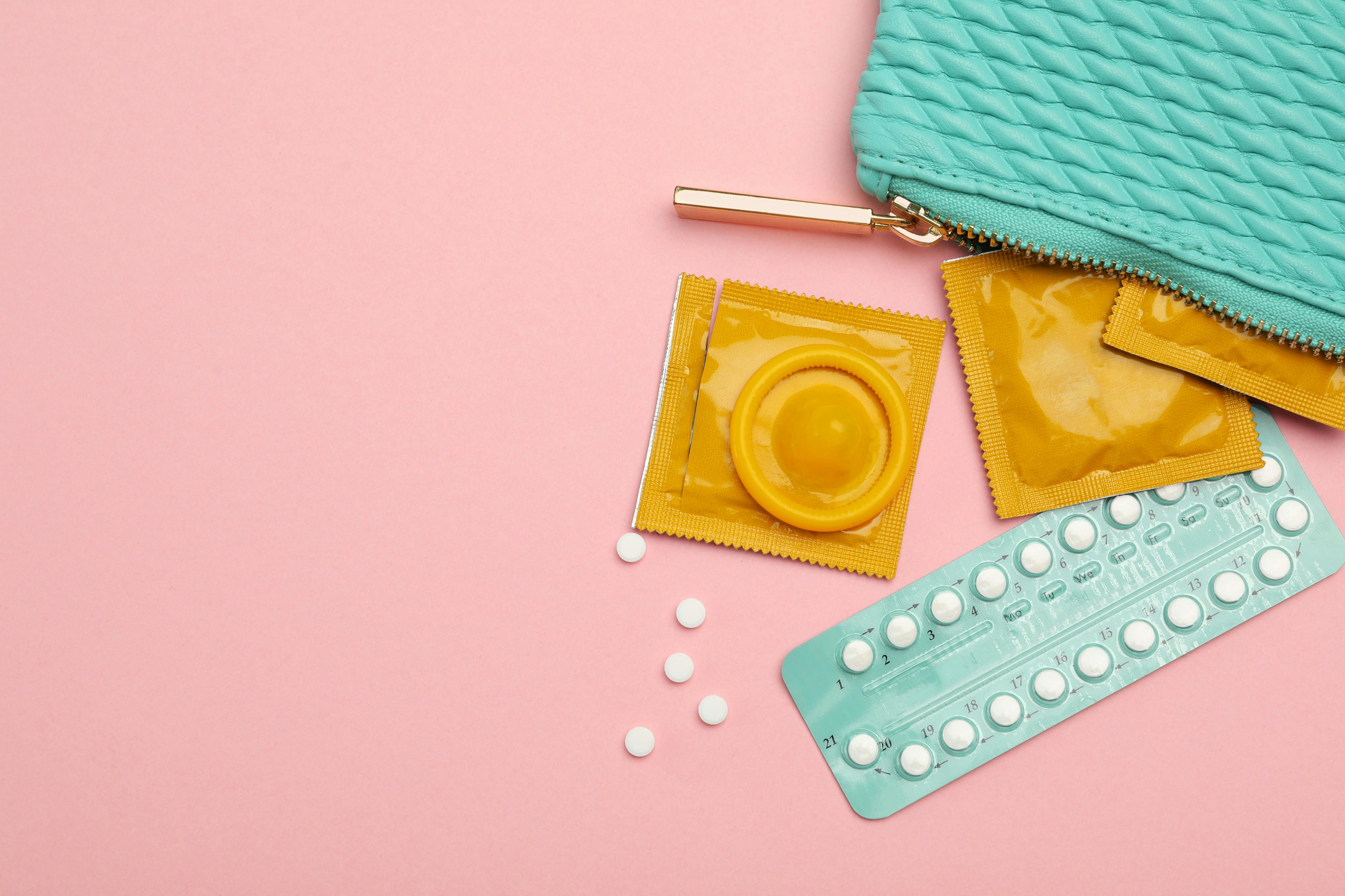 Condoms and birth control pills in purse on pink background, top view with space for text. Safe sex - Image credit: New Africa | stock.adobe.com