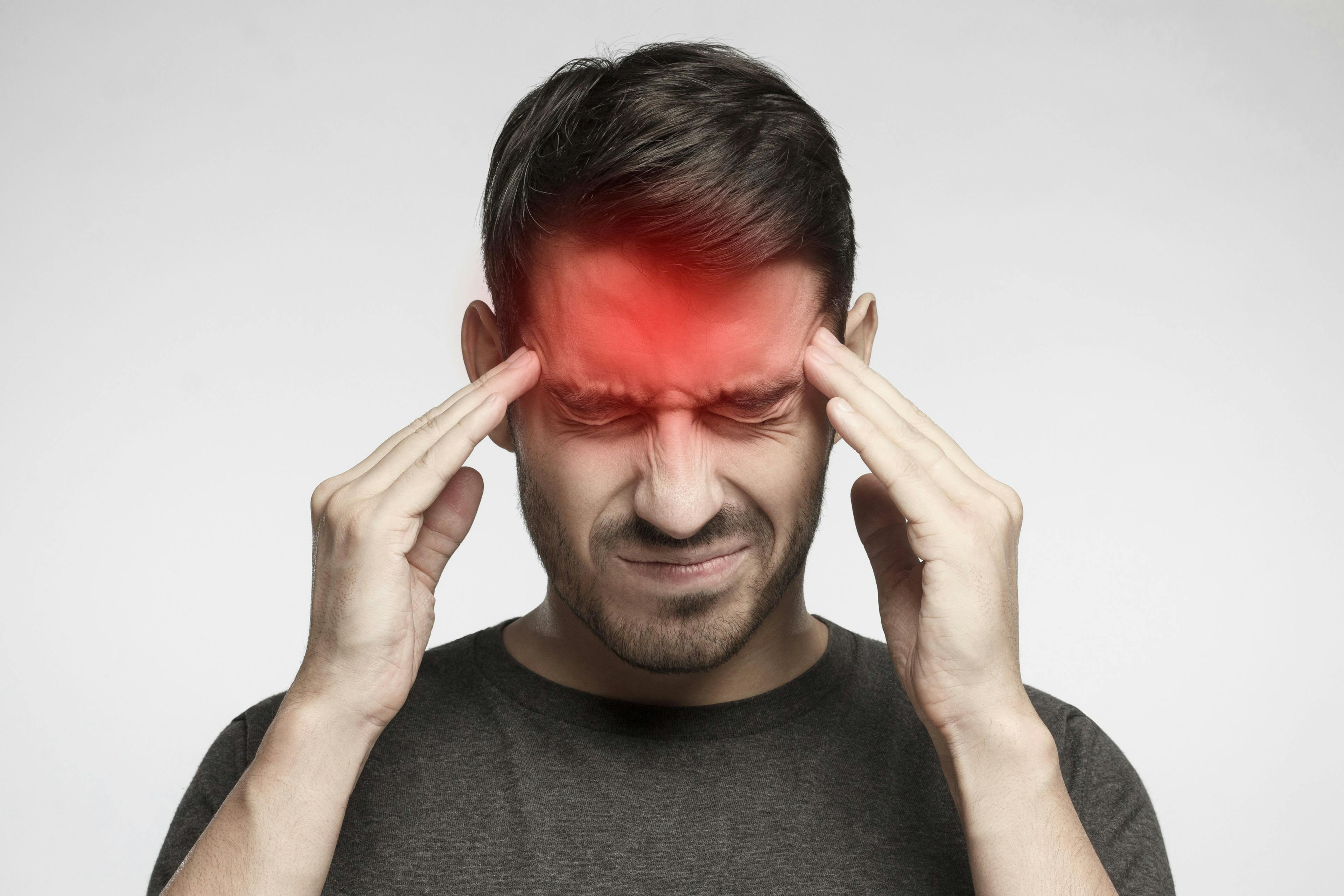 Portrait of young man isolated on gray background, suffering from severe headache, pressing fingers to temples with closed eyes. Credit: Damir Khabirov - stock.adobe.com