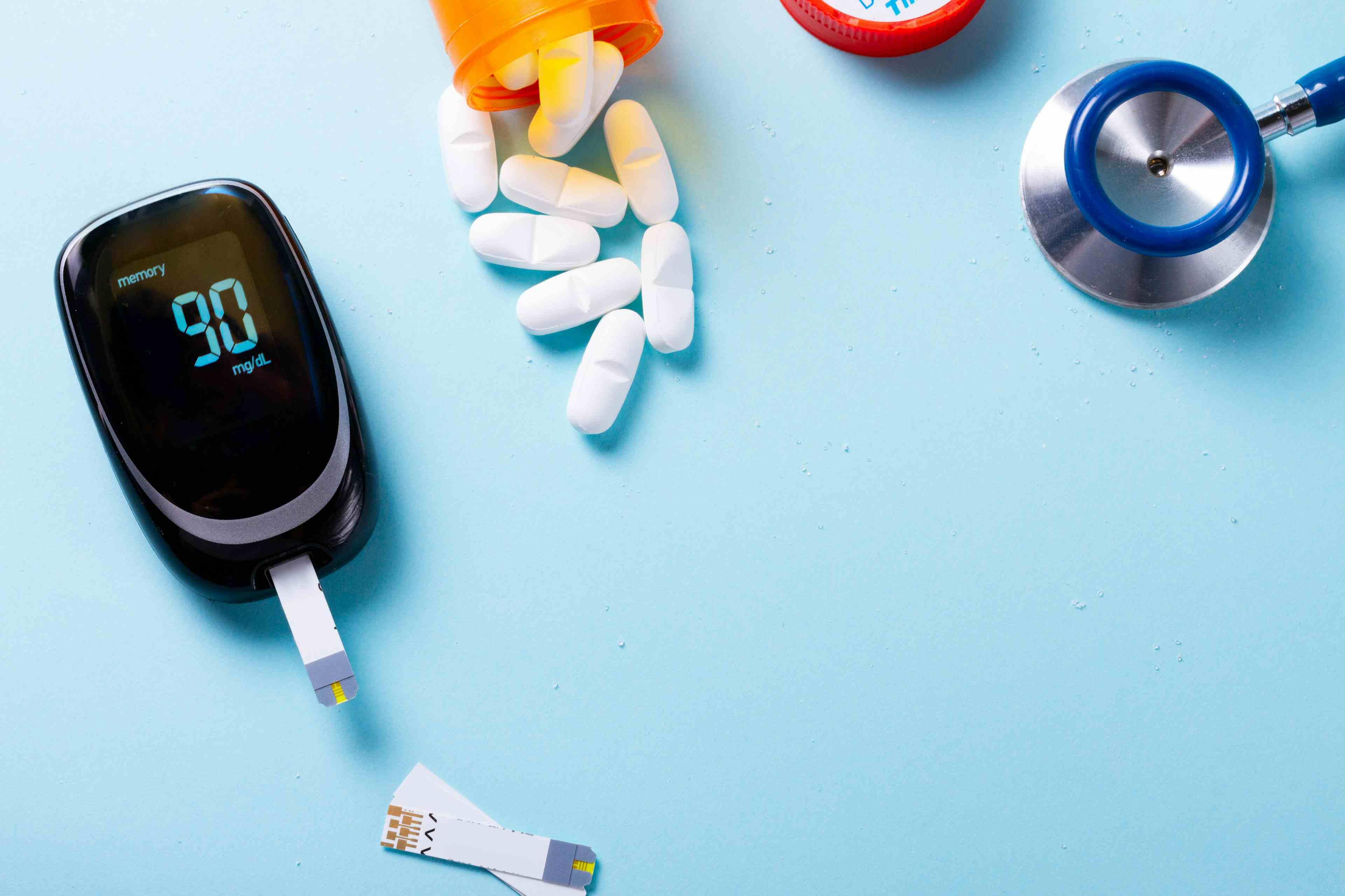 White pills in orange bottle with blood glucose meter on blue background 