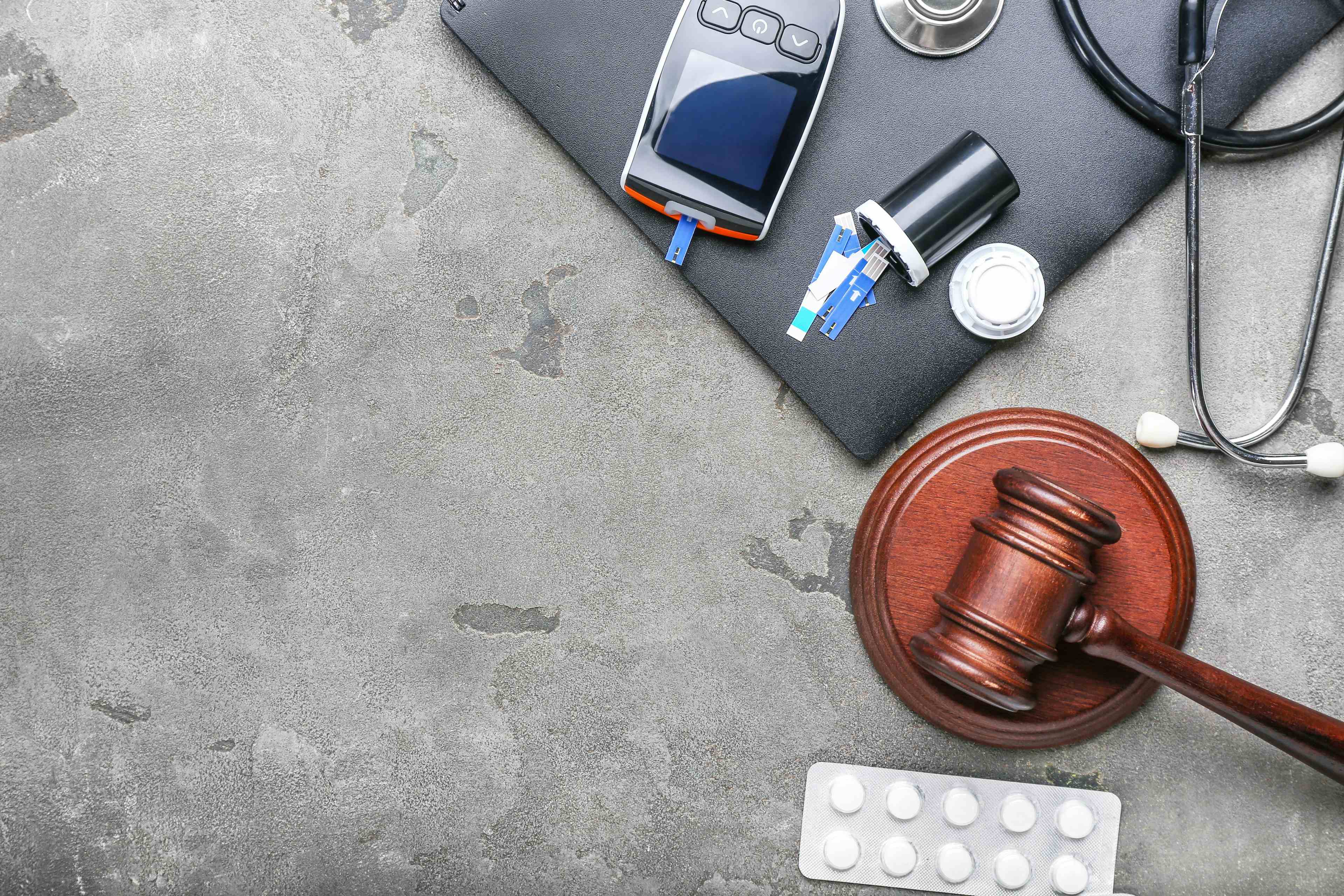 Judge gavel, pills, glucometer and stethoscope on grey background