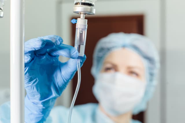 Nurse connecting an intravenous drip in hospital room.