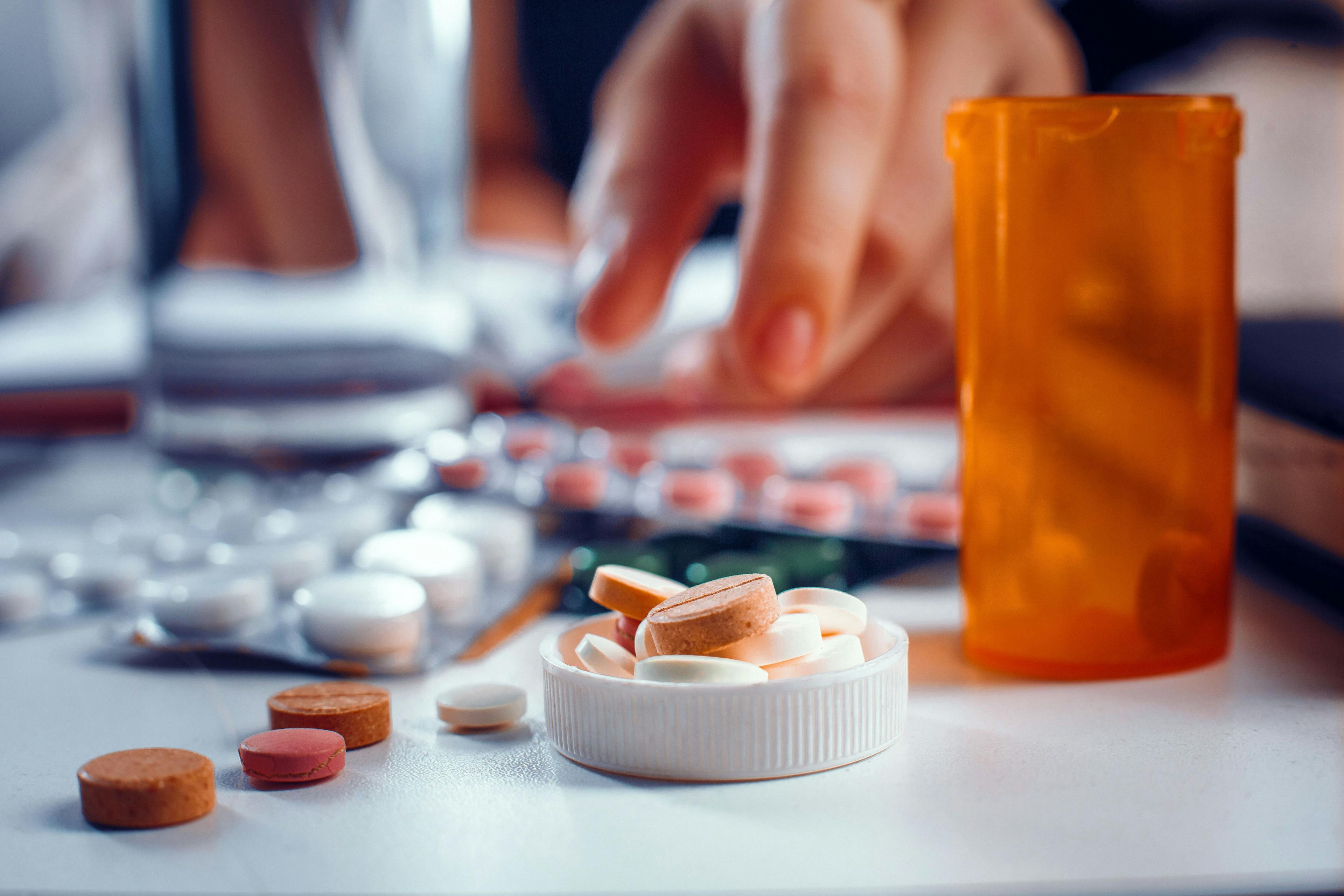 Blurred hand reaches for the orange pills laying on the table. Many other tablets laying blurred on the table near the spilled pills - Image credit: Svyatoslav Lypynskyy | stock.adobe.com 