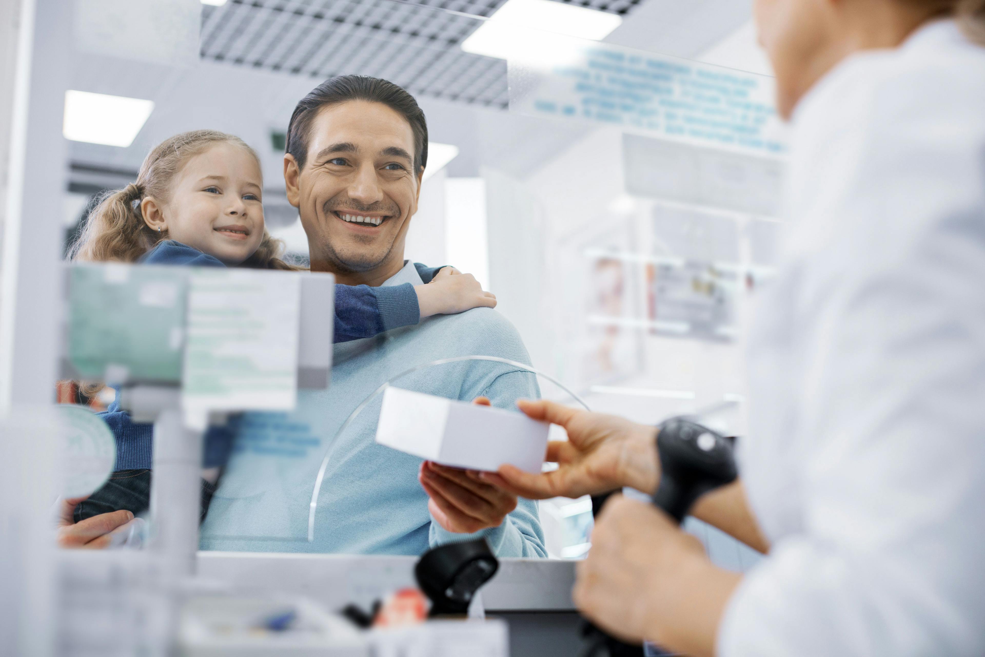 Low angle of female pharmacist transmitting medication and jolly man holding girl - Image credit: zinkevych | stock.adobe.com