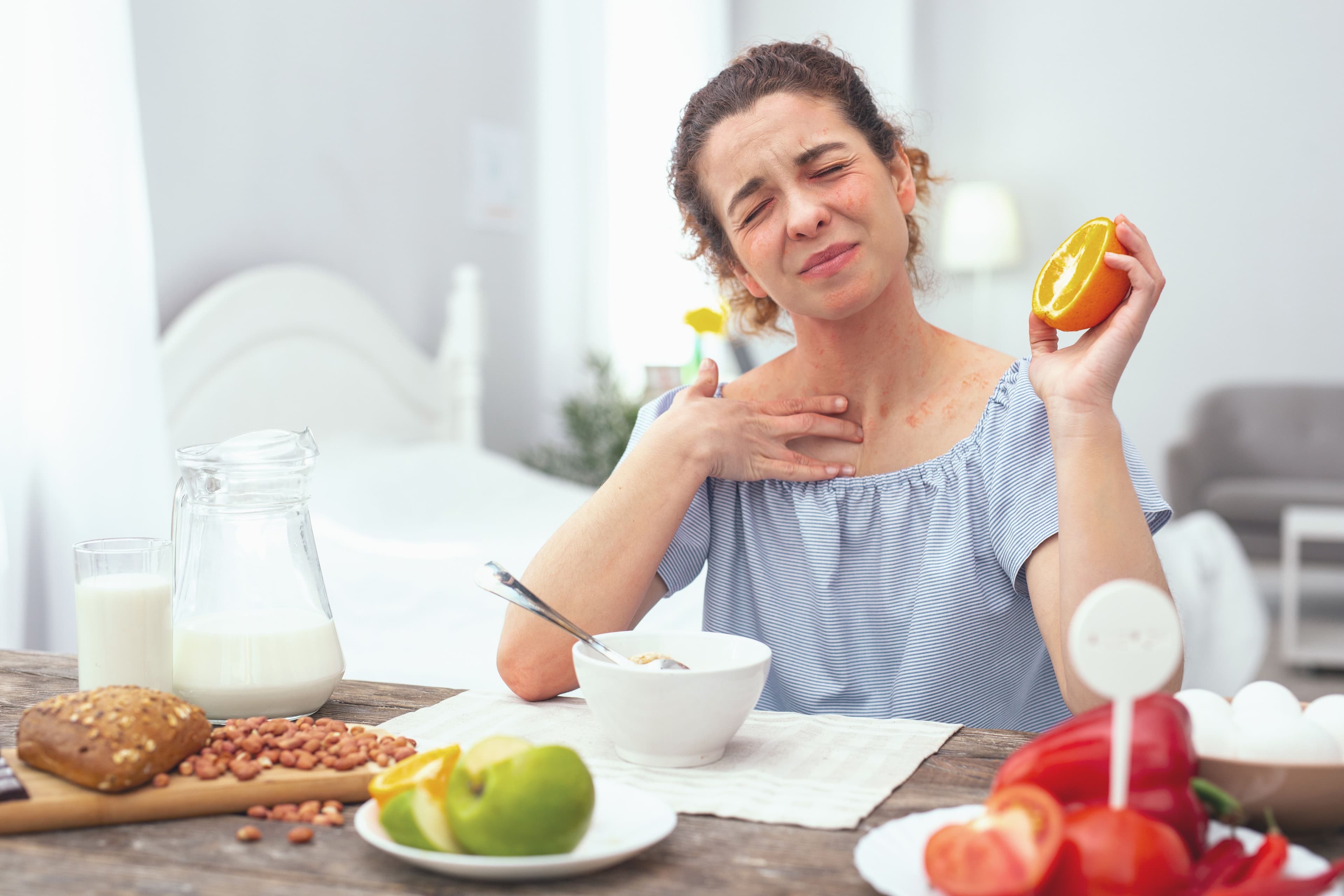 Young woman looking sore and getting an allergic rash while eating an orange during her dinner