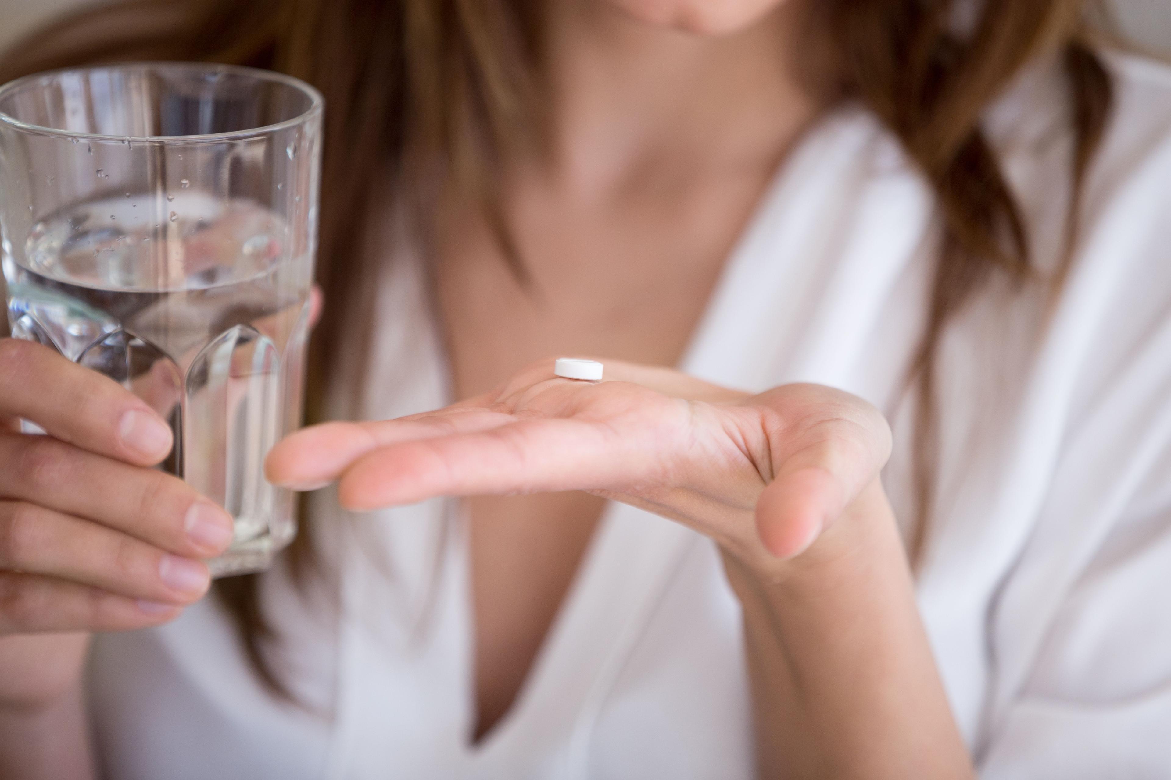 Woman holding pill and glass of water in hands taking emergency medicine, supplements or antibiotic antidepressant painkiller medication to relieve pain, meds side effects concept, close up