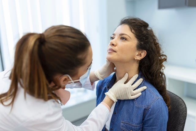 Endocrinologist examining throat of young woman in clinic. 