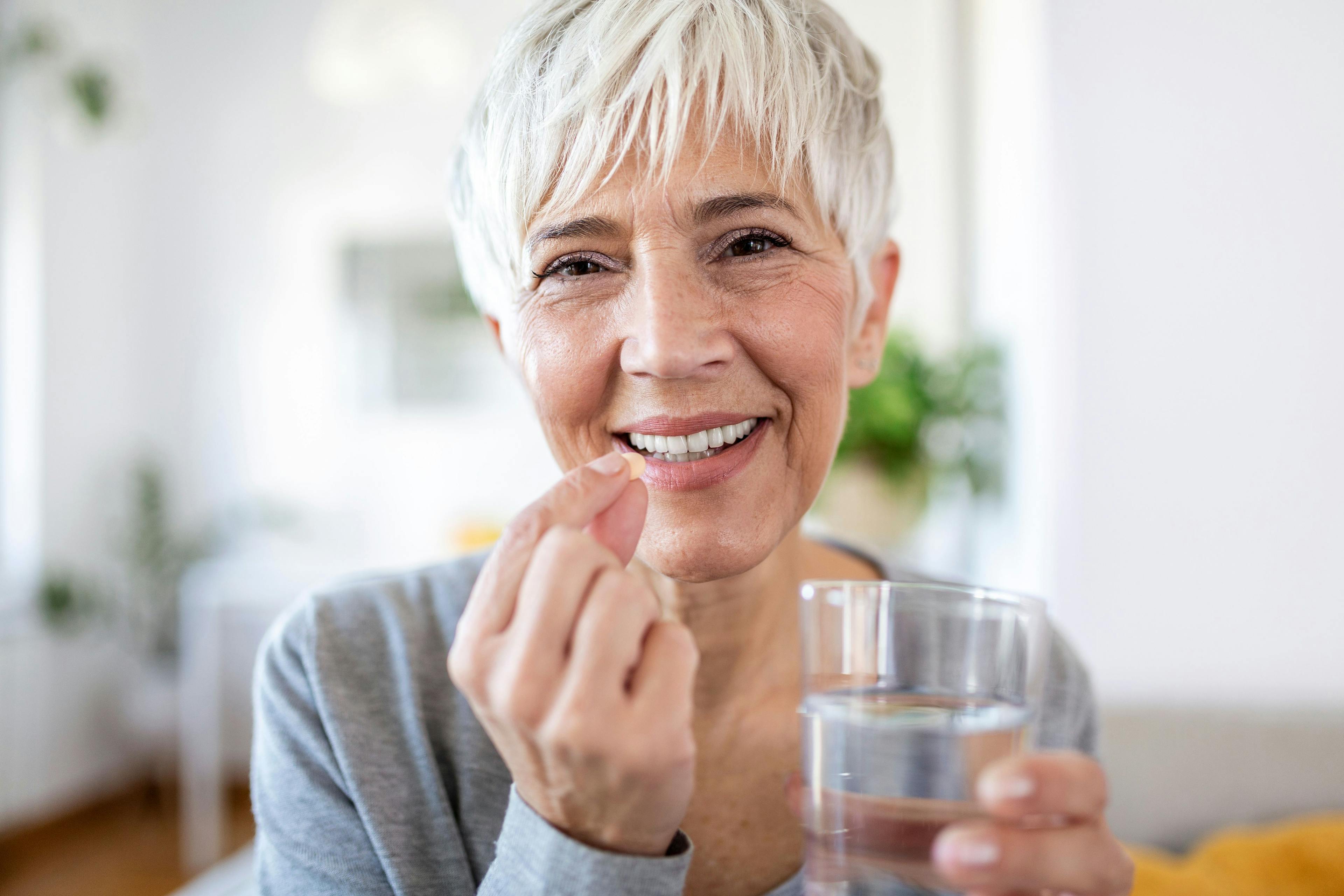 Head shot portrait happy woman holds pill glass of water, takes daily medicine vitamin D, omega 3 supplements, skin hair nail strengthen and beauty, medication for health care concept - Image credit: Graphicroyalty | stock.adobe.com 