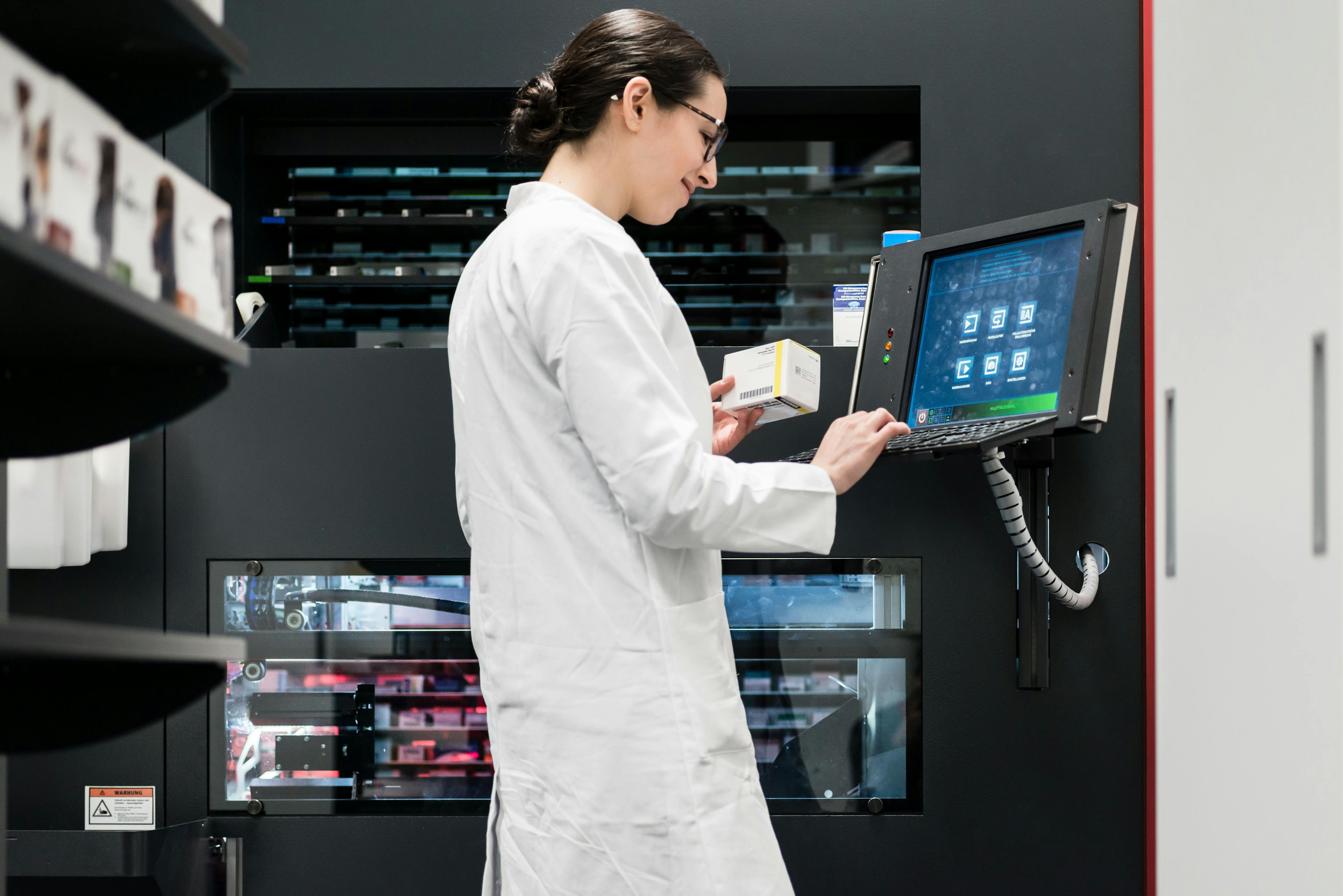Female pharmacist using a computer while managing the drug stock in a contemporary pharmacy with modern technology and automation