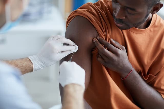 Close up of unrecognizable male nurse injecting vaccine in shoulder of African-American man during covid vaccination in clinic or hospital