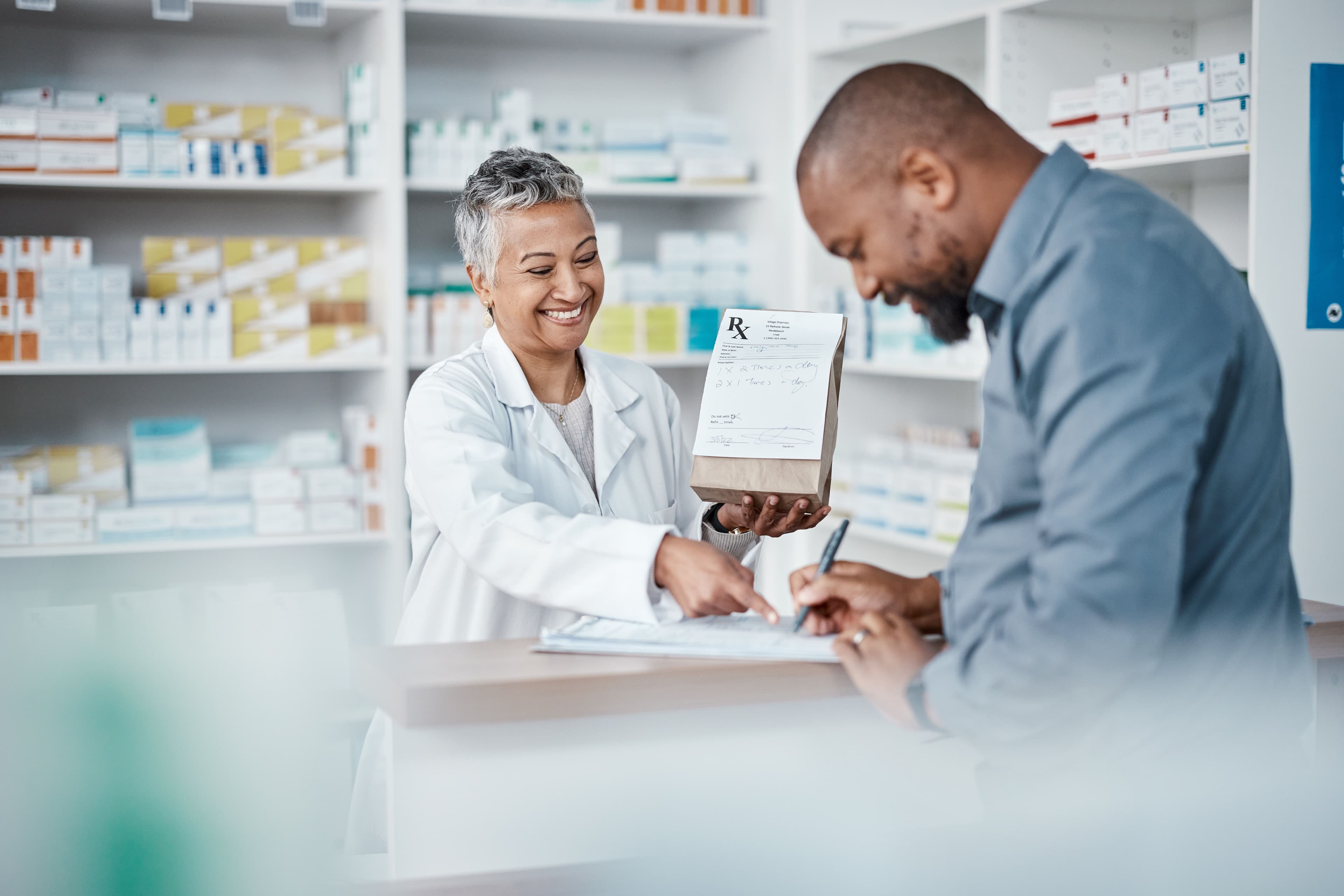 Medicine, shopping or pharmacist with customer writing personal or medical information in pharmacy. Consulting, pills or happy senior doctor helping or speaking to black man or sick African customer - Image credit: C Daniels/peopleimages.com | stock.adobe.com