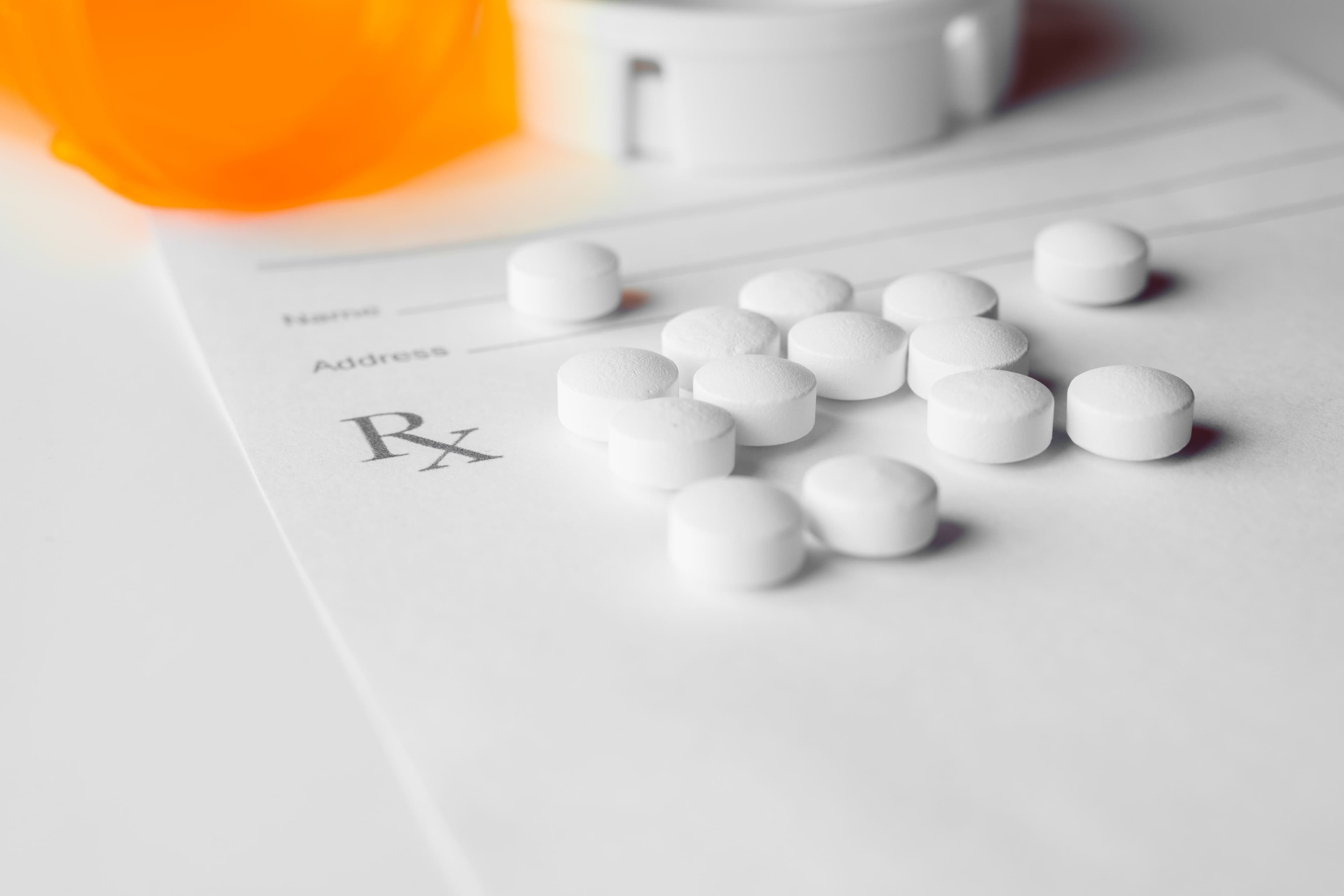 White prescription pills laying on rx pad on white background