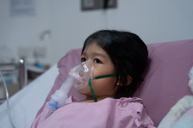 A little Asian girl has an oxygen mask and breathing through a nebulizer at the hospital