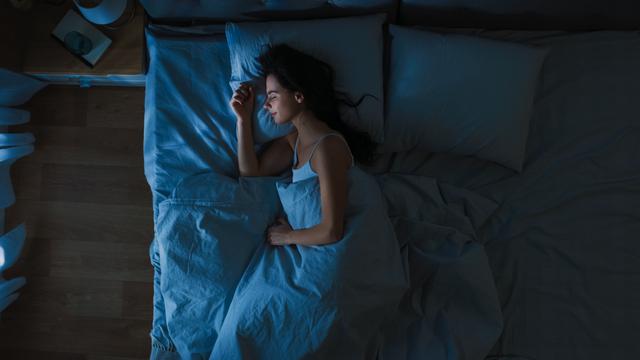 Top View of Beautiful Young Woman Sleeping Cozily on a Bed in His Bedroom at Night. Blue Nightly Colors with Cold Weak Lamppost Light Shining Through the Window - Image credit: Gorodenkoff | stock.adobe.com 