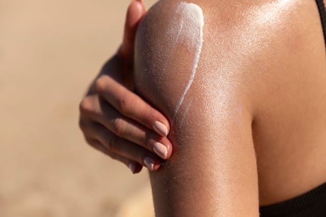 Young woman applying sun cream or sunscreen on her tanned shoulder to protect her skin from the sun. Shot on a sunny day with blurry sand in the background  - Image credit: Lea | stock.adobe.com 