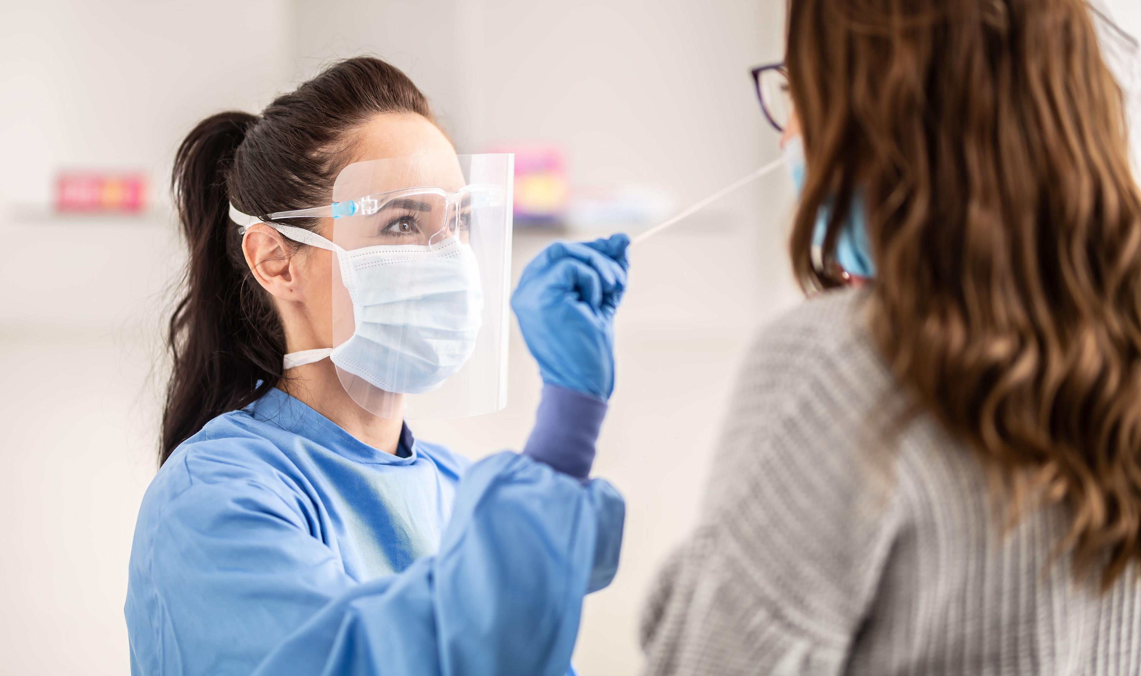 Female medical staff worker wearing protective equipment takes sample from nose of a patient to antigen test for coronavirus