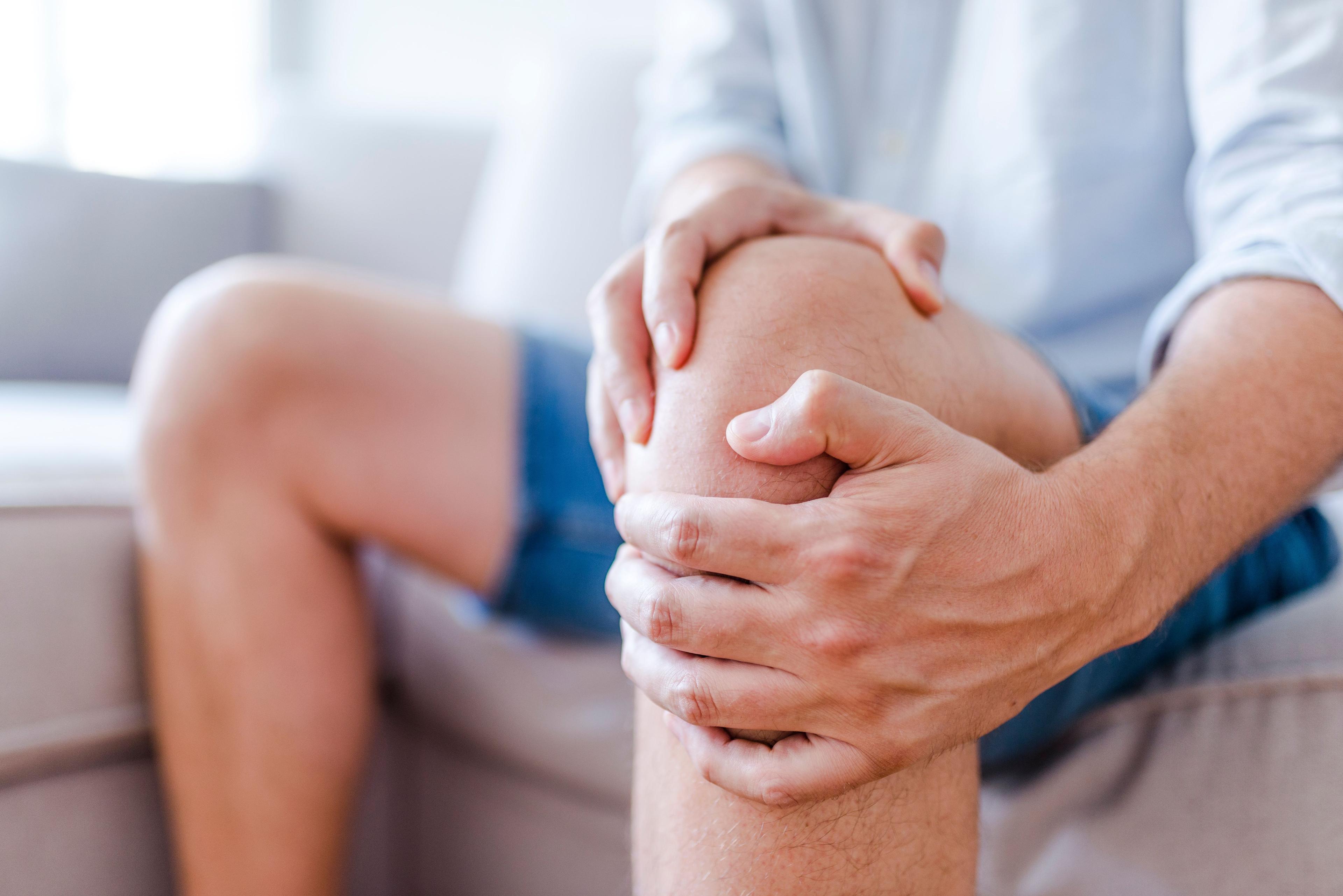 Man suffering from knee pain sitting on sofa.