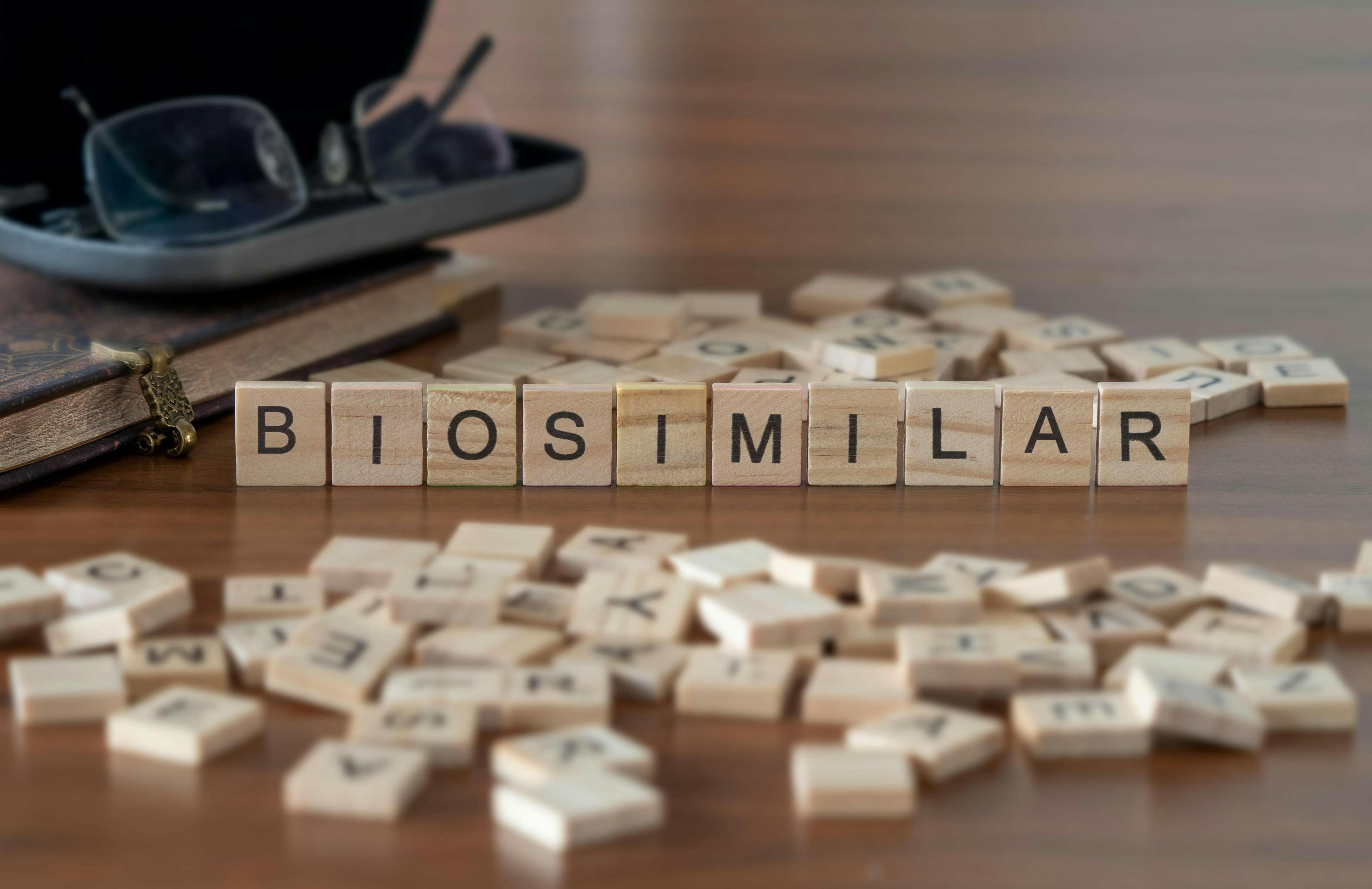 The word "biosimilar" represented by wooden letter tiles on a wooden table with glasses and a book.